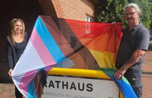 Die Buchholzer Gleichstellungsbeauftragte Yvonne Bodendiek mit Hausmeister Oliver Biere mit der Regenbogenflagge, die jetzt gehisst vor dem Rathaus hängt. Foto: Stadt Buchholz